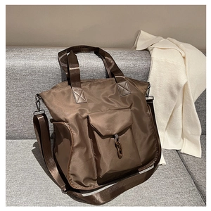 Detail view of large brown nylon tote bag with metal chain on a soft grey sofa