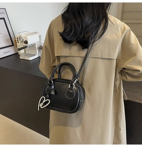 Detail of black bowling bag with white stitching and heart charm on a trench coat