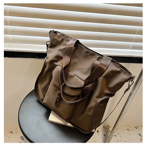 Detail of a dark brown nylon tote bag featuring a front pocket with a metal chain decoration