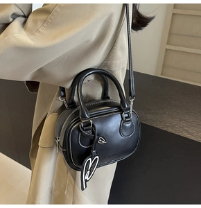 Fashionable black leather bowling bag with white stitching shown on a camel trench coat