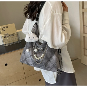 Detail of grey quilted tote bag featuring pearl chain and plush cloud charm accessory
