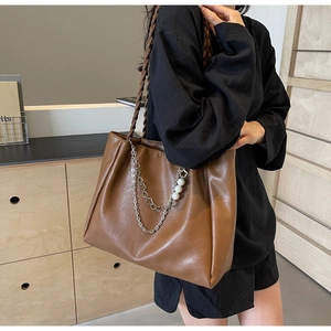 Close-up of brown tote bag with woven strap and decorative pearl chain on model