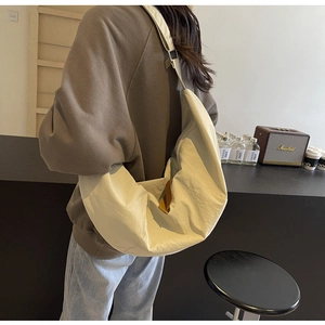 Detailed back view of a cream crescent nylon crossbody bag on model in a cafe setting