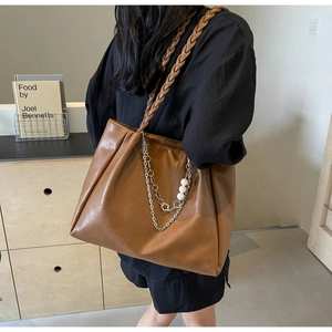 Detail of brown tote bag with woven strap and silver chain featuring pearl charms
