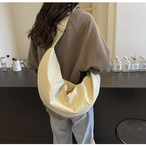 Model wearing a large cream nylon crescent bag with adjustable strap in a cafe setting