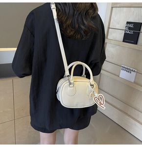 Crossbody view of a cream mini Boston bag with double handles and heart-shaped charm