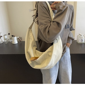 Large beige nylon crescent bag shown on a model in a cozy cafe setting for daily wear