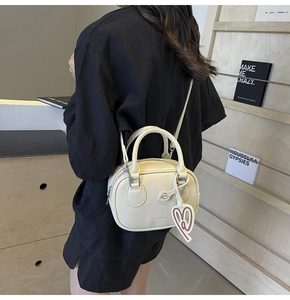 Detail of cream bowling bag with LANCE & SHUAI text and B leather charm on a model