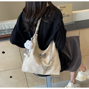 Detail of beige quilted tote bag with pearl chain, silver bow, and plush cloud charm