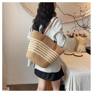 Detail view of woven beach tote with white stripes and brown leather straps on shoulder