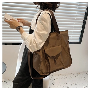 Large brown nylon tote bag with front flap pocket and dual straps shown on a model