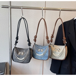 Detail of strap design on suede shoulder bags with pearl chains and bow accents