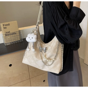 Detail of cream quilted tote bag featuring silver bow, pearl chain and plush charm