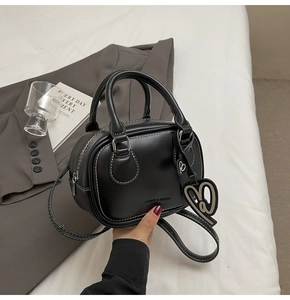 Detail of black bowling bag with white stitching, heart charm and adjustable strap