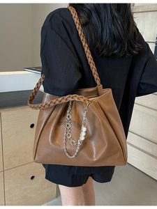 Brown leather tote bag with woven strap and pearl chain charm, modeled on shoulder