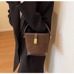 Detail of a brown matte suede bucket bag featuring a gold metal clasp and elegant handle