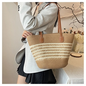Detail of a large woven straw tote bag with brown leather straps worn on the shoulder
