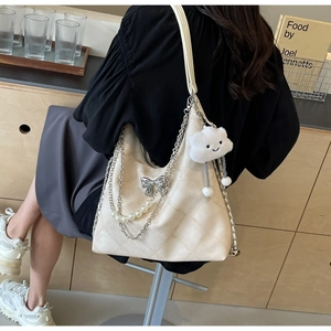 Detail of cream quilted tote bag with pearl chain and bow worn by a model in a cafe
