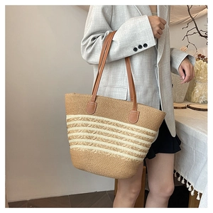 Detail of striped straw tote bag featuring brown leather shoulder straps and woven texture
