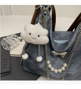 Soft white fluffy cloud charm with striped legs hanging on a denim backpack