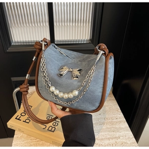 Detail of blue denim hobo bag with silver bow, pearl chain and knotted leather strap