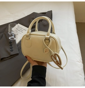 Detail of cream white leather bowling bag with heart charm and brand embossing