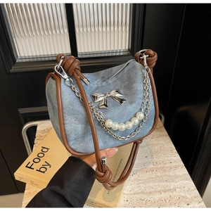 Detail of blue denim shoulder bag with brown leather trim and silver butterfly ornament