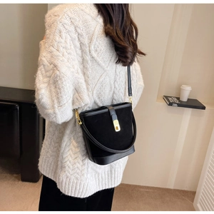 Detail of black matte suede bucket bag with gold clasp shown on a white cable knit sweater