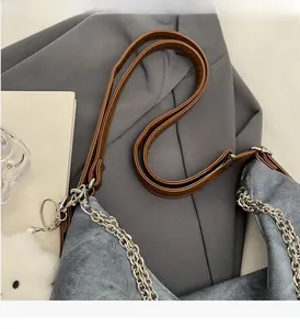 Detail of blue denim bag with brown leather strap, silver chain, and cloud charm