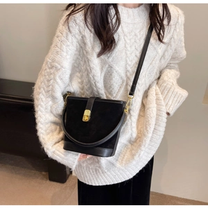 Detail of black bucket bag with gold clasp and textured suede leather on a white sweater