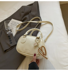 Detail of cream bowling bag with heart charm and adjustable strap on minimal background