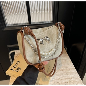 Detailed close-up of beige suede handbag with bow accent and elegant pearl chain strap