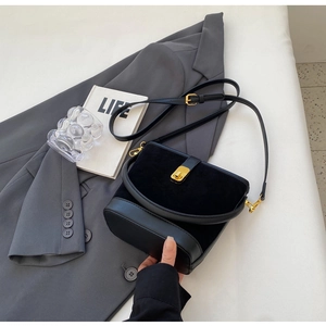 Close-up of black bucket bag showing suede texture, gold buckle, and slim strap