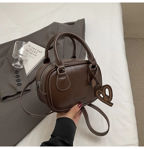 Detail of dark brown leather handbag featuring contrast stitching and heart charm accessory