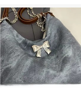 Detail of metallic bow buckle on denim backpack with silver chain and leather strap
