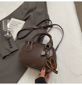 Detail of a dark brown leather bowling bag with heart charm on a grey suit jacket