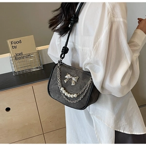 Dark grey suede shoulder bag with ribbon design and pearl chain shown on model