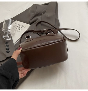 Detail of a brown leather mini Boston bag featuring white stitching and brand logo