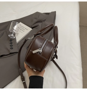 Detail view of dark brown leather bowling bag with white contrast stitching and silver zipper