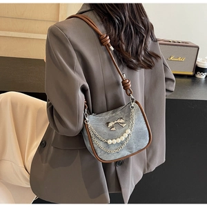 Detail of gray denim shoulder bag with pearl chain, metal bow and brown leather strap