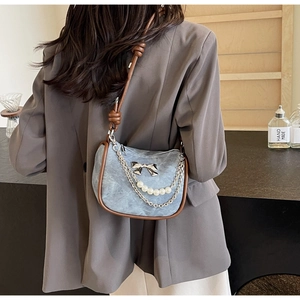 Detail of denim shoulder bag featuring silver metal bow and pearl chain decorative straps