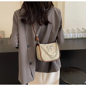 Detail of crossbody bag featuring pearl chain, silver bow buckle and tied leather strap