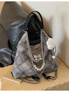 Grey quilted tote bag with silver bow accent and pearl chain strap on stone display