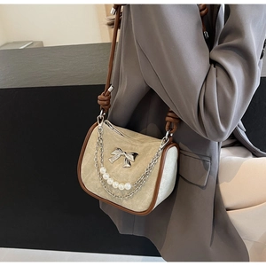 Detail of beige suede baguette bag with pearl chain, brown trim and metal bow accent