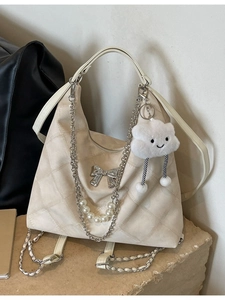 Beige quilted tote bag with silver bow and pearl chain on stone background