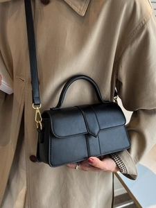 Elegant black leather handbag with pointed flap and gold hardware, worn with a trench coat