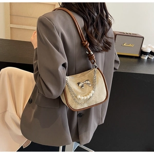 Close-up of beige suede handbag with pearl chain and bow metallic detail
