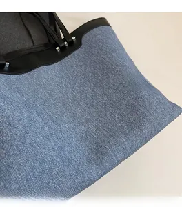 Close-up of denim tote bag with black leather trim and silver metal buckle hardware