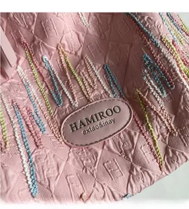 Detailed close-up of pink quilted fabric with colorful embroidery and a leather logo tag