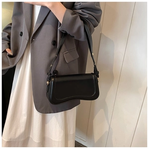 Detail of minimalist black underarm bag with unique wavy curved base on model in grey suit